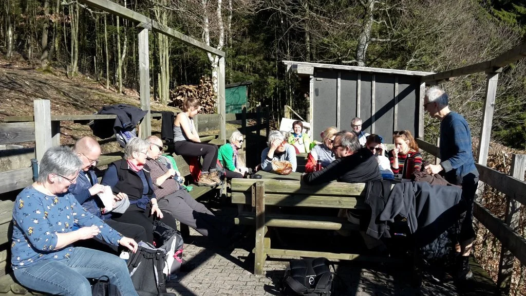 Viele Wandernde sitzen bei sonnigem Wetter an Holztischen im Freien, einige essen. | © DAV Dortmund