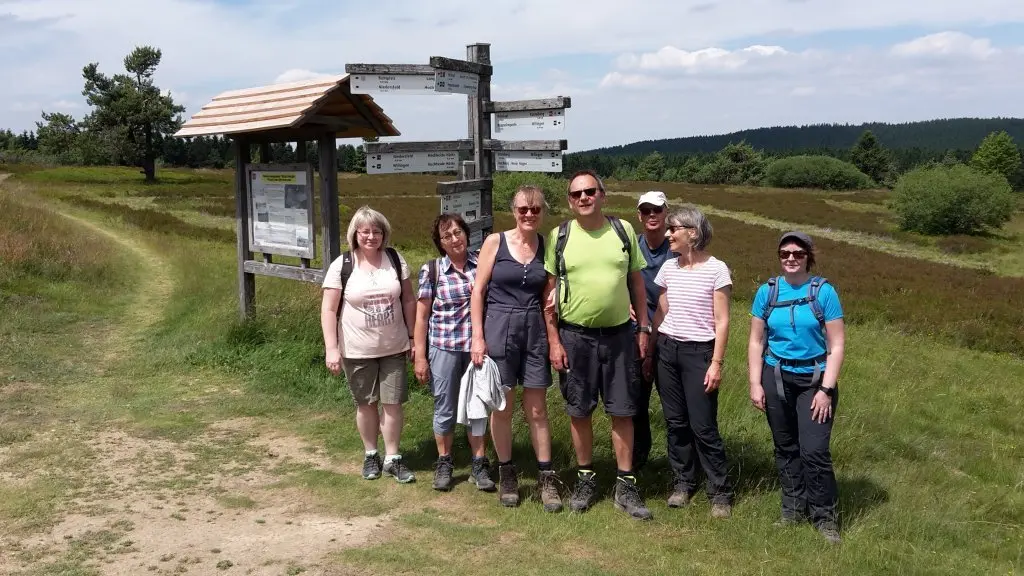 Acht Wandernde stehen vor einem großen Wanderschild auf einem Feldweg. | © DAV Dortmund