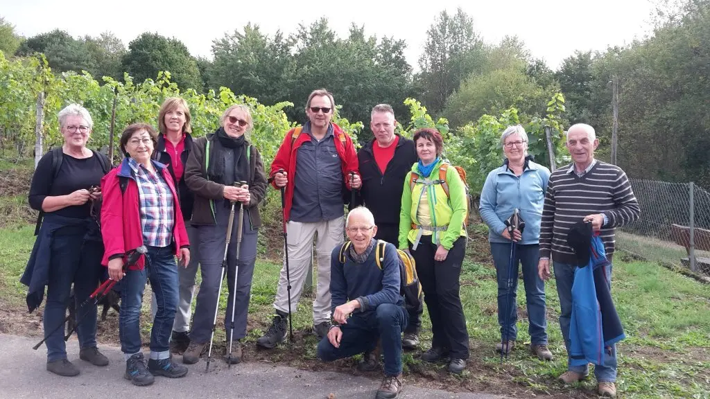 Zehn Wandernde stehen lächelnd vor einer grünen Weinberglandschaft. | © DAV Dortmund