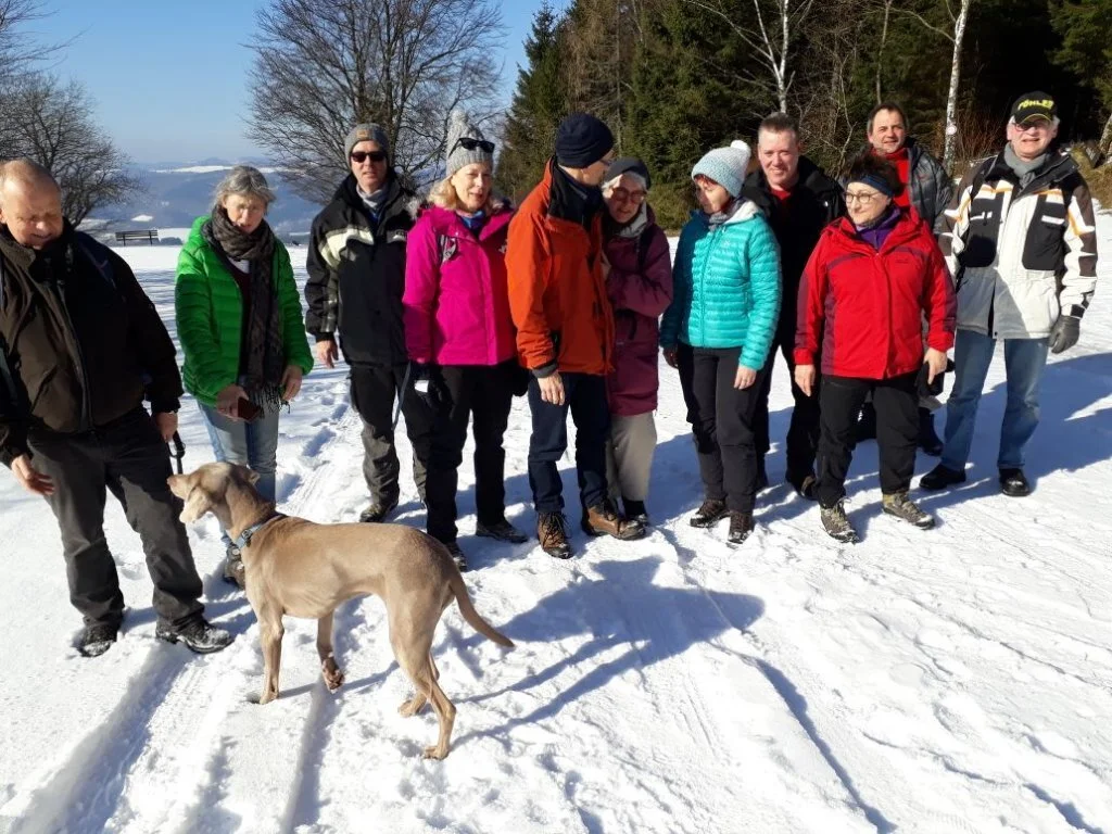 Eine Gruppe von 13 Personen mit Hund steht im Sonnenschein auf einem verschneiten Weg. | © DAV Dortmund