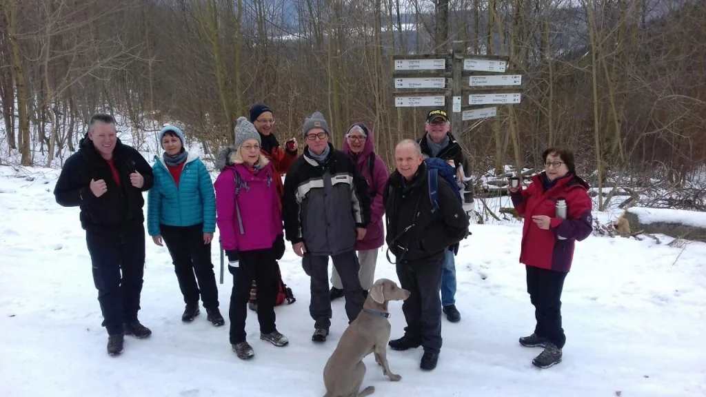 Gruppe von Wandernden mit Hund steht im Schnee vor mehreren Wegweisern. | © DAV Dortmund