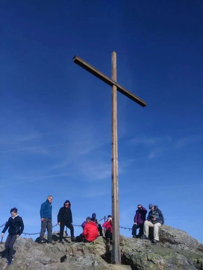 Wandergruppe auf felsigem Gipfel mit großem Holzkreuz und tiefblauem Himmel. | © DAV Dortmund