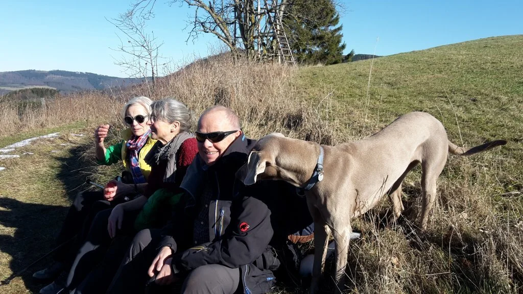 Vier Personen sitzen am Wegrand auf einer Bank, ein großer Hund steht daneben. | © DAV Dortmund