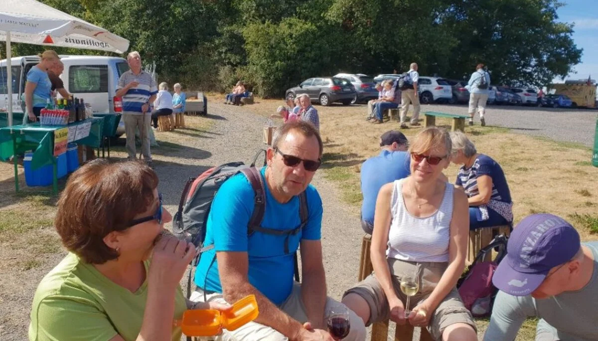 Mehrere Personen sitzen auf Holzbänken bei einem Weinstand und unterhalten sich. | © DAV Dortmund
