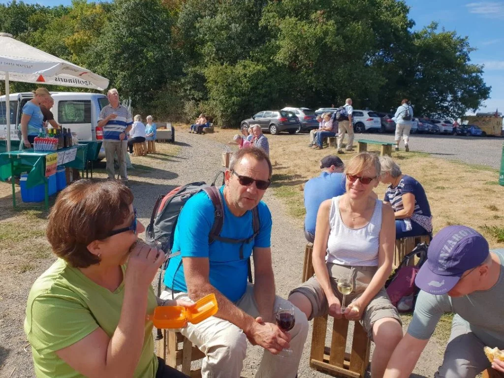 Mehrere Personen sitzen auf Holzbänken bei einem Weinstand und unterhalten sich. | © DAV Dortmund