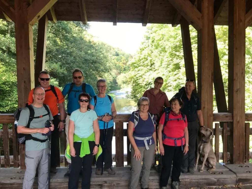 Wanderer mit Rucksäcken und Hund stehen auf einer überdachten Holzbrücke mit Blick auf einen Fluss. | © DAV Dortmund