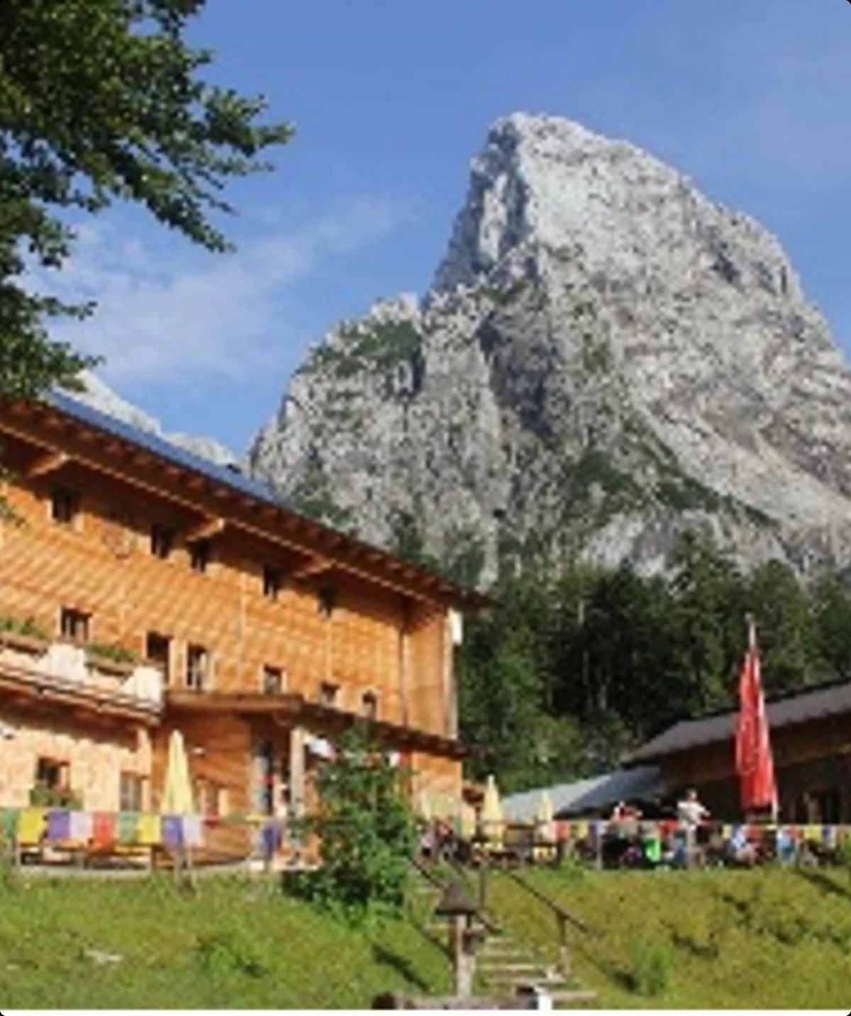 Große Berghütte mit Holzfassade in den Alpen, im Hintergrund ein steiler Felsgipfel unter blauem Himmel. | © DAV Dortmund
