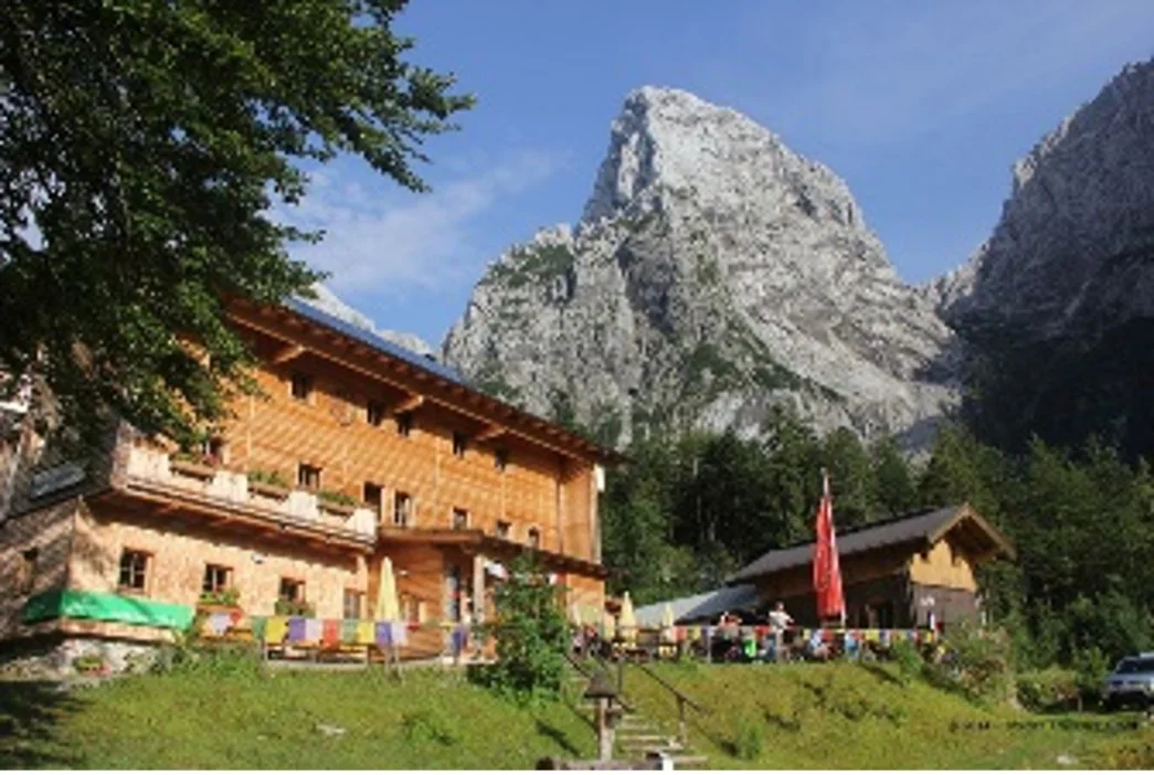 Große Berghütte mit Holzfassade in den Alpen, im Hintergrund ein steiler Felsgipfel unter blauem Himmel. | © DAV Dortmund