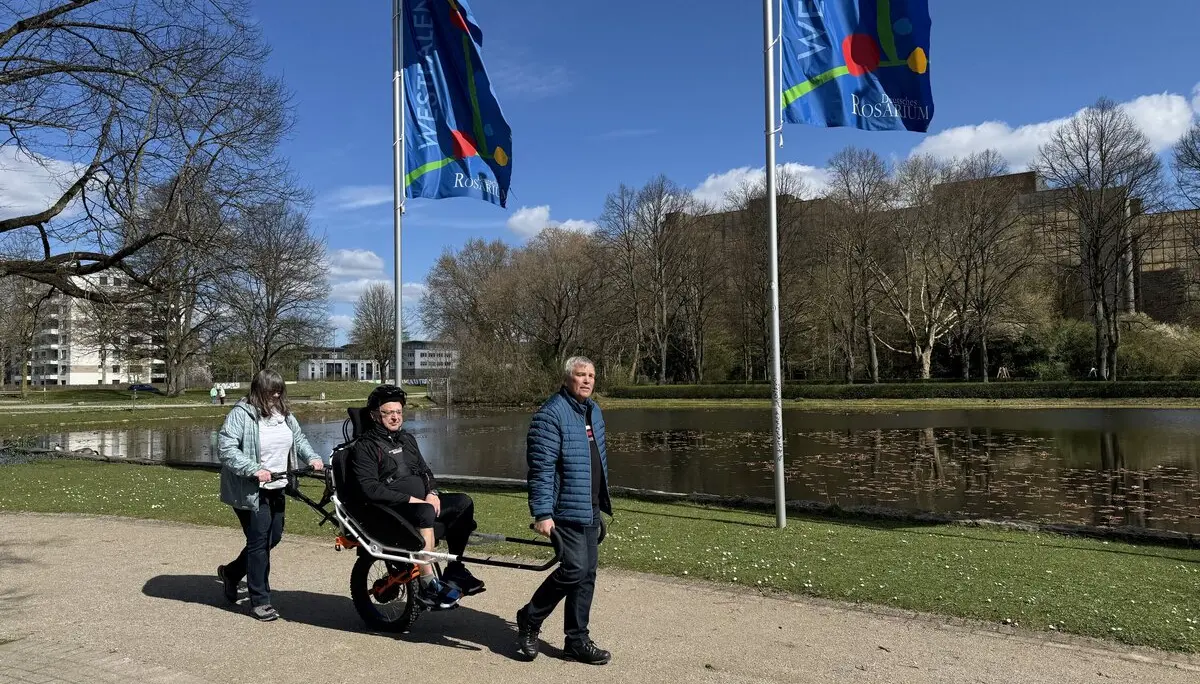 Drei Personen unterwegs mit einer Joëlette am Seeufer mit wehenden Fahnen. | © DAV Dortmund