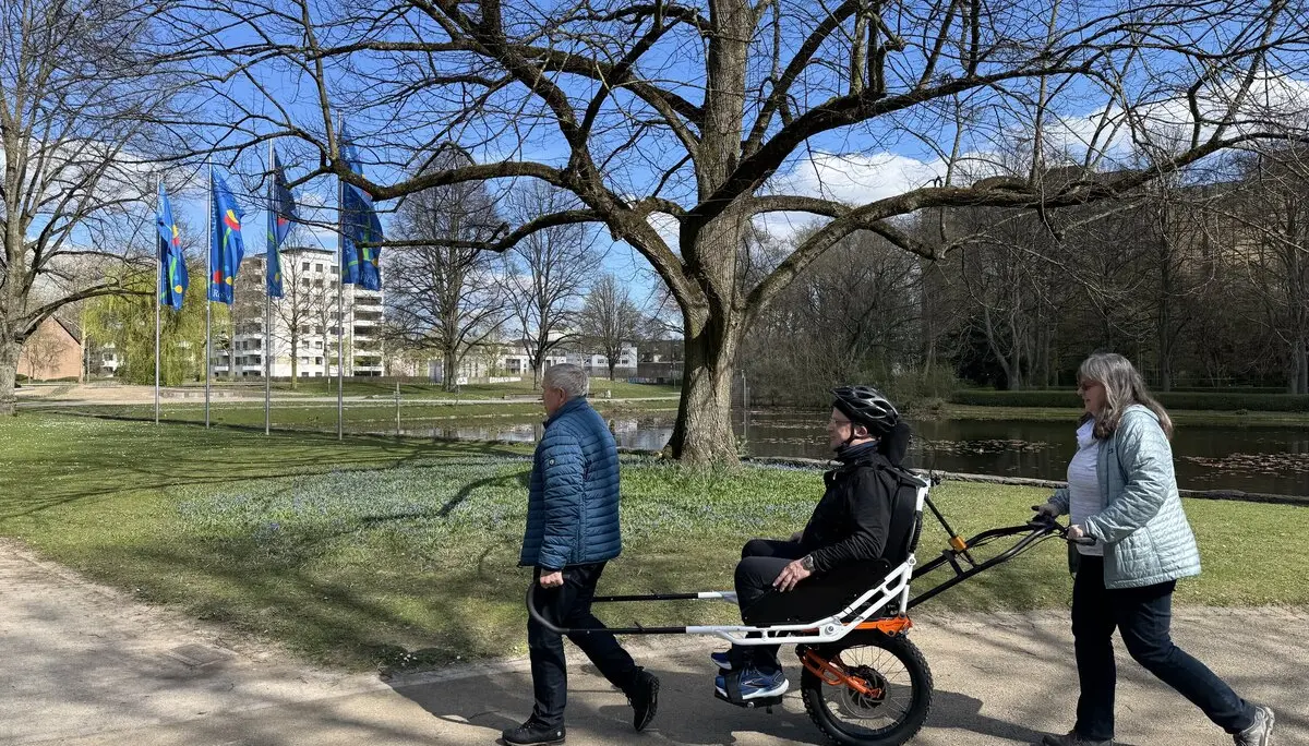 Person sitzt in einer geländegängigen Joëlette, zwei Begleitpersonen helfen beim Transport auf einem Parkweg. | © DAV Dortmund