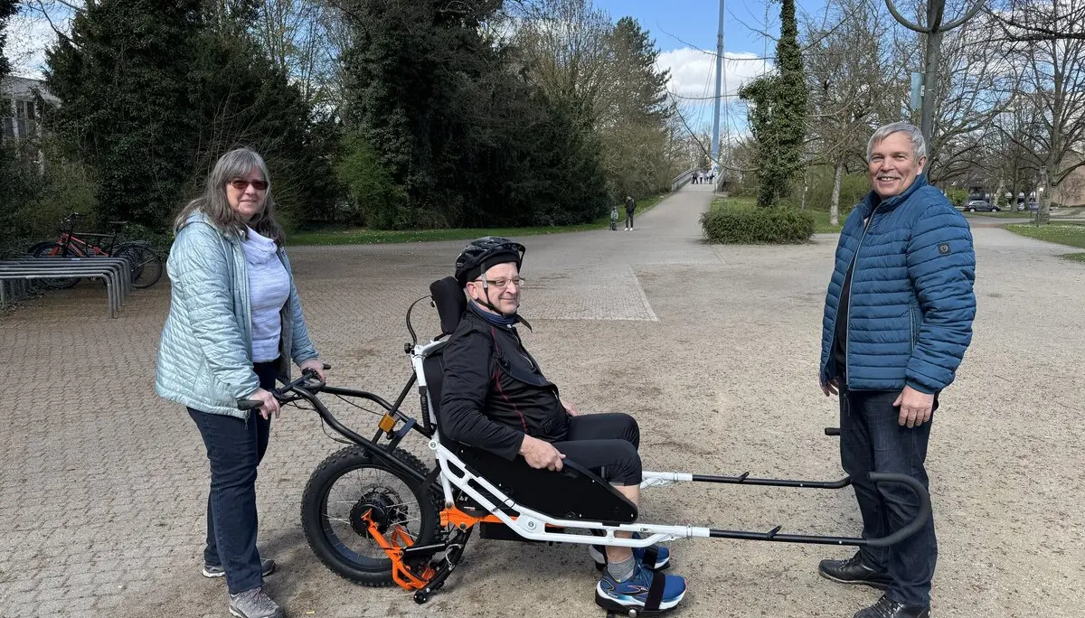 Person sitzt in einer geländegängigen Joëlette, zwei Begleitpersonen helfen beim Transport auf einem Parkweg. | © DAV Dortmund