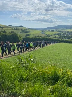 Lange Reihe von Wander*innen zieht sich durch eine hügelige grüne Landschaft. | © DAV Dortmund
