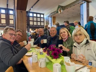 Personengruppe sitzt lachend an einem Tisch in einer Hütte mit Getränken. | © DAV Dortmund