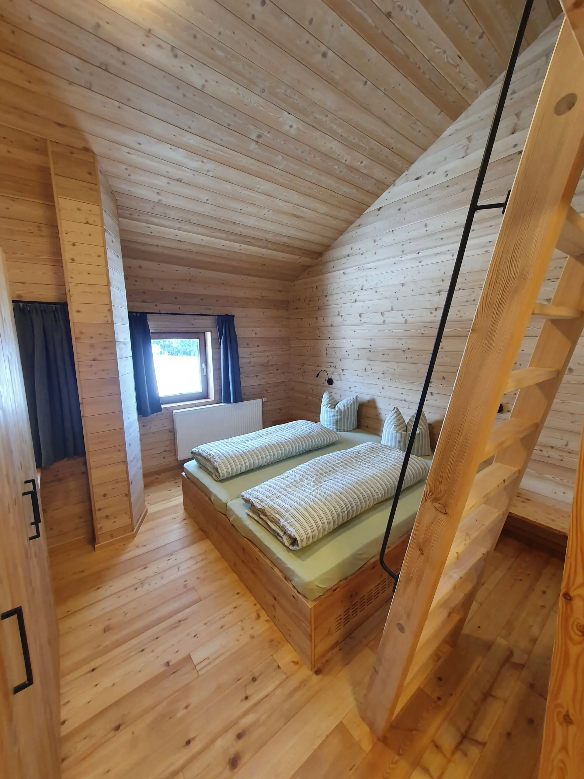 Ein helles Zimmer mit Holzwänden und Doppelbett, darüber eine Galerie mit Holzleiter erreichbar. | © DAV Dortmund