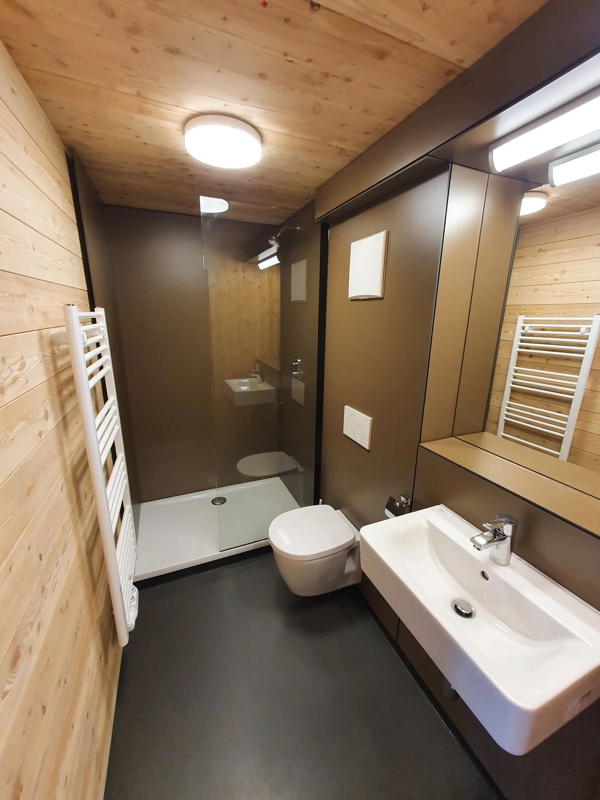 Badezimmer mit bodengleicher Dusche, WC, Waschbecken und heller Beleuchtung in Holzoptik. | © DAV Dortmund