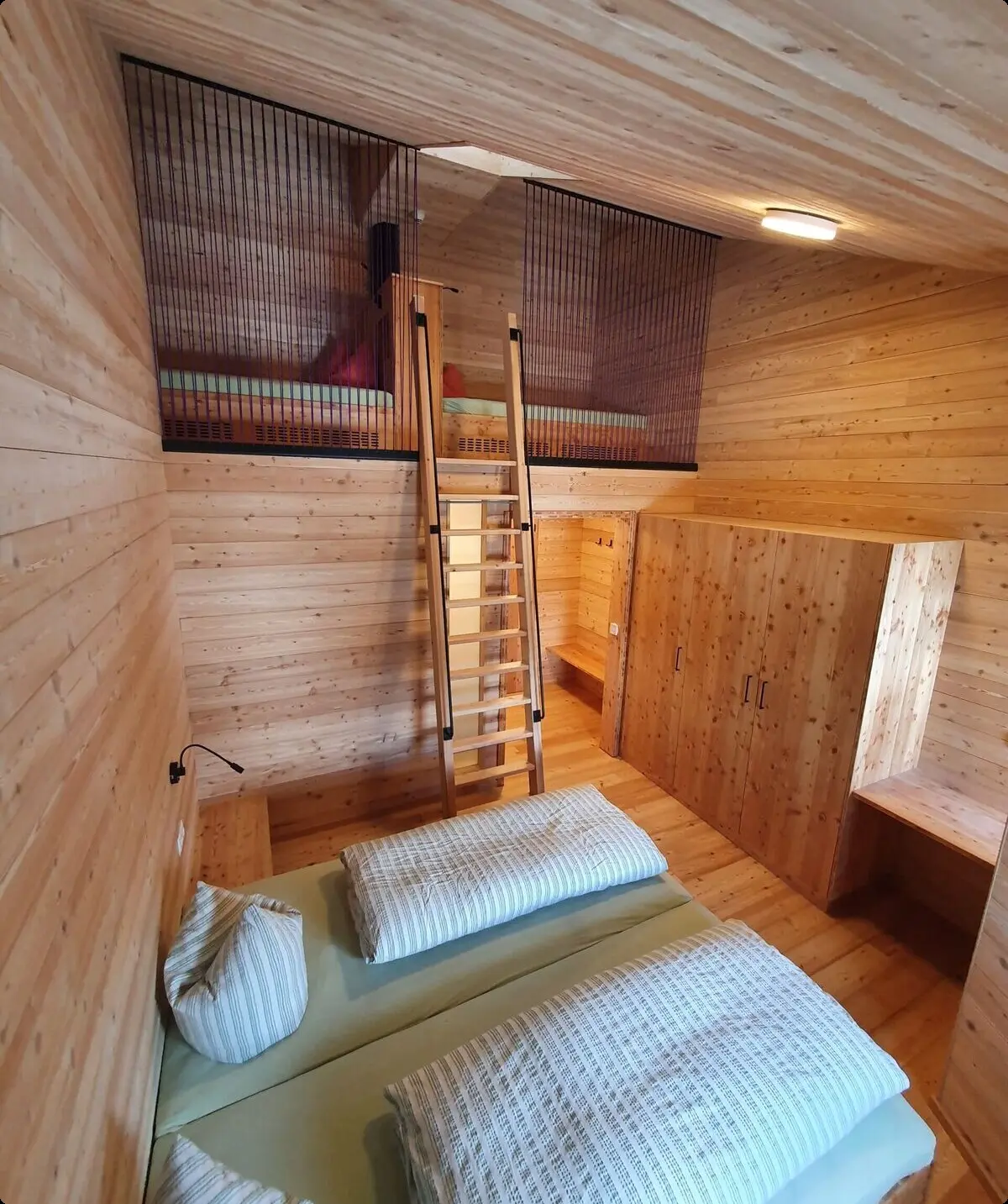 Doppelbett in einem Zimmer mit Holzverkleidung und offener Galerie mit zusätzlicher Schlafmöglichkeit. | © DAV Dortmund