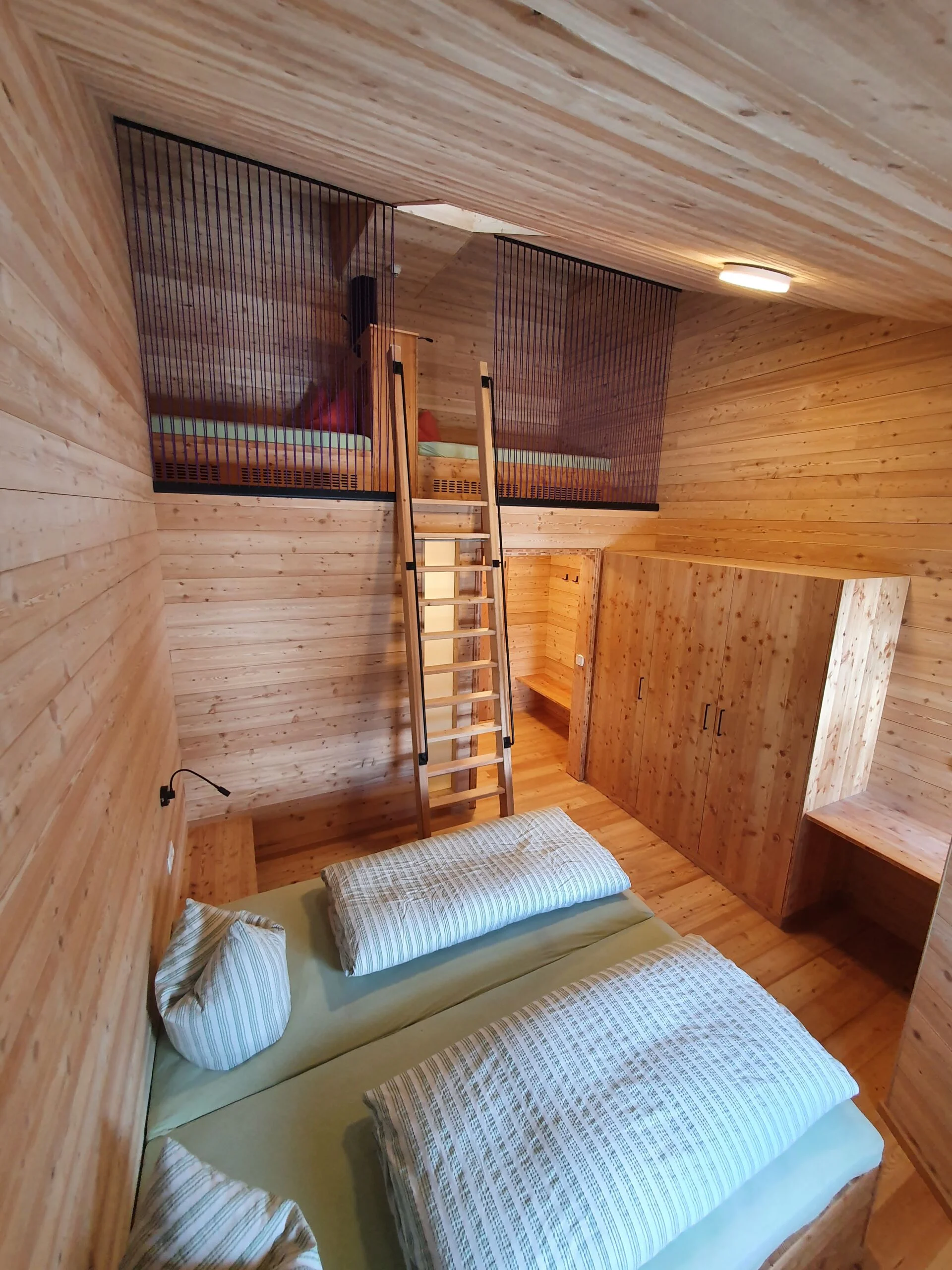 Doppelbett in einem Zimmer mit Holzverkleidung und offener Galerie mit zusätzlicher Schlafmöglichkeit. | © DAV Dortmund