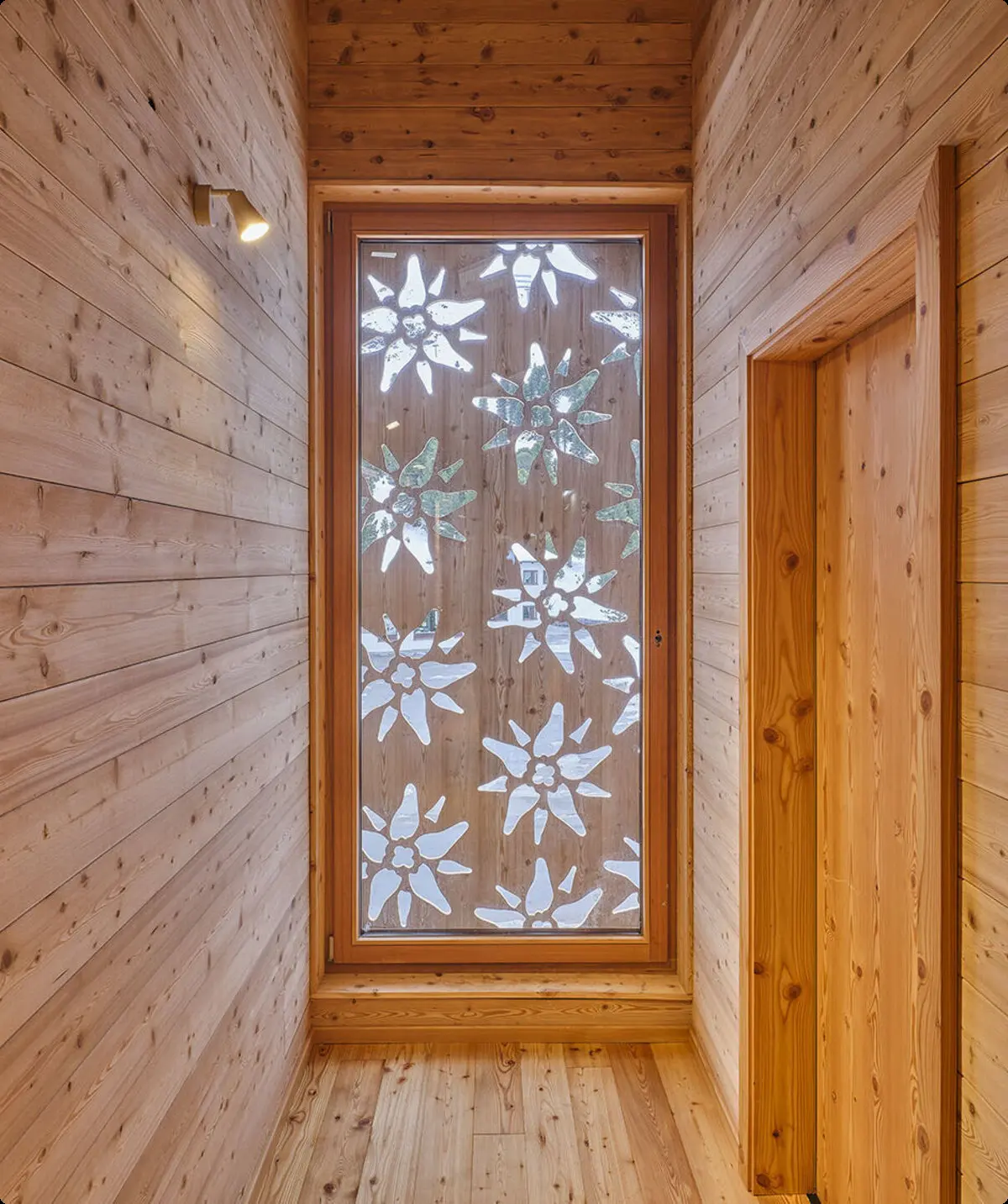 Großes Fenster mit Dekor aus Edelweißblüten am Ende eines Holzflurs in einer Berghütte. | © DAV Dortmund