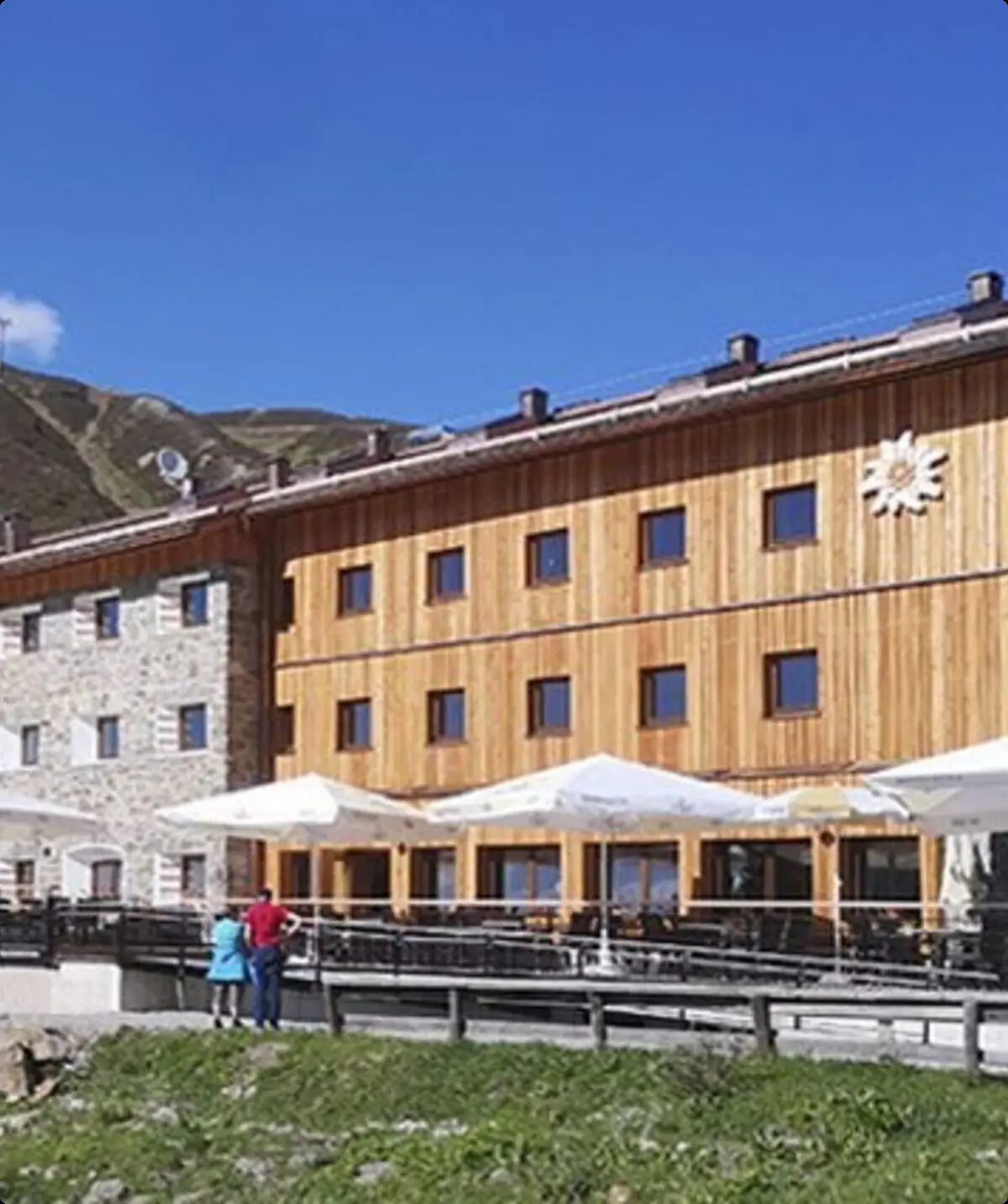 Die Dortmunder Hütte mit Holzfassade, Sonnenschirmen und Bergpanorama im Hintergrund. | © DAV Dortmund