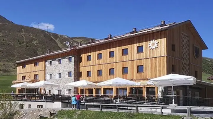 Die Dortmunder Hütte mit Holzfassade, Sonnenschirmen und Bergpanorama im Hintergrund. | © DAV Dortmund