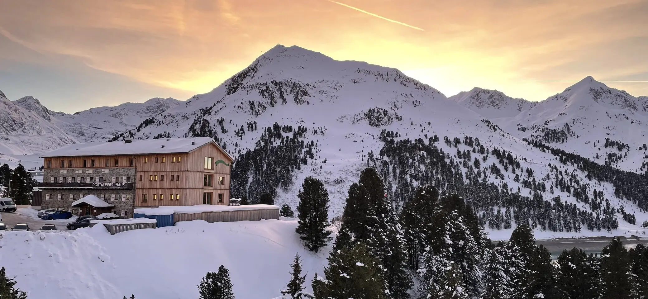 Berghütte vor verschneiten Gipfeln, dahinter ein farbenprächtiger Sonnenuntergang. | © H. Schimmelfelder