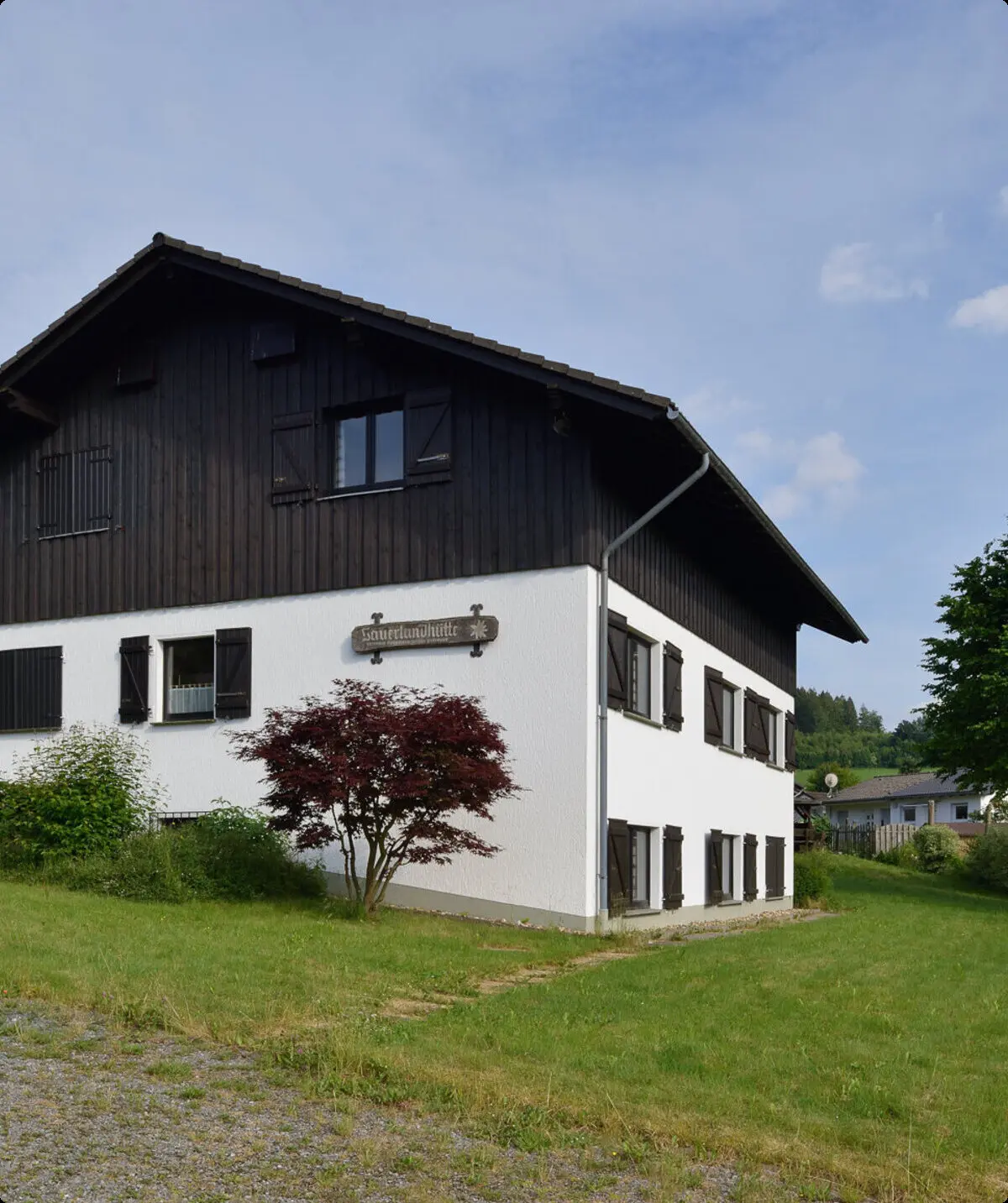 Eine zweistöckige Berghütte mit weißer Fassade und dunklem Holzaufsatz in grüner Umgebung. | © DAV Dortmund
