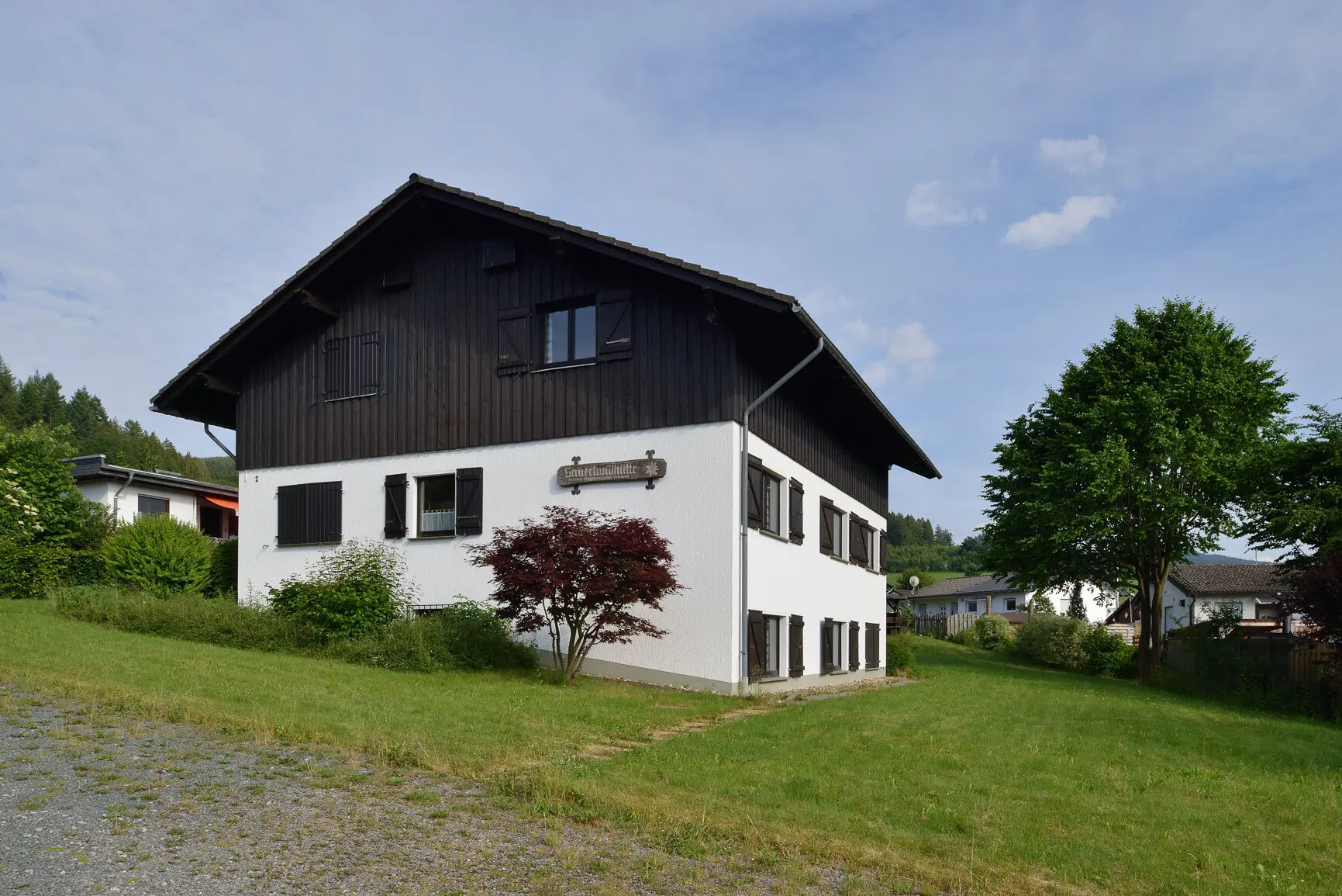 Eine zweistöckige Berghütte mit weißer Fassade und dunklem Holzaufsatz in grüner Umgebung. | © DAV Dortmund