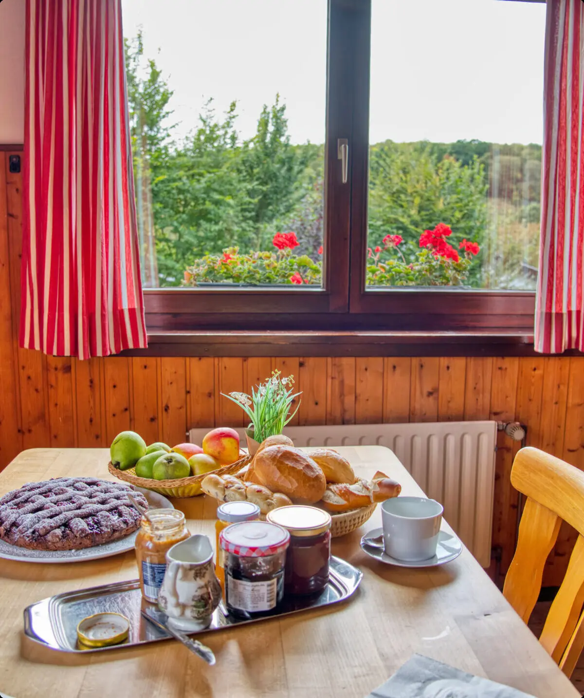 Ein gedeckter Frühstückstisch mit Marmelade, Brot und Obst vor einem Fenster mit Blumen. | © DAV Dortmund