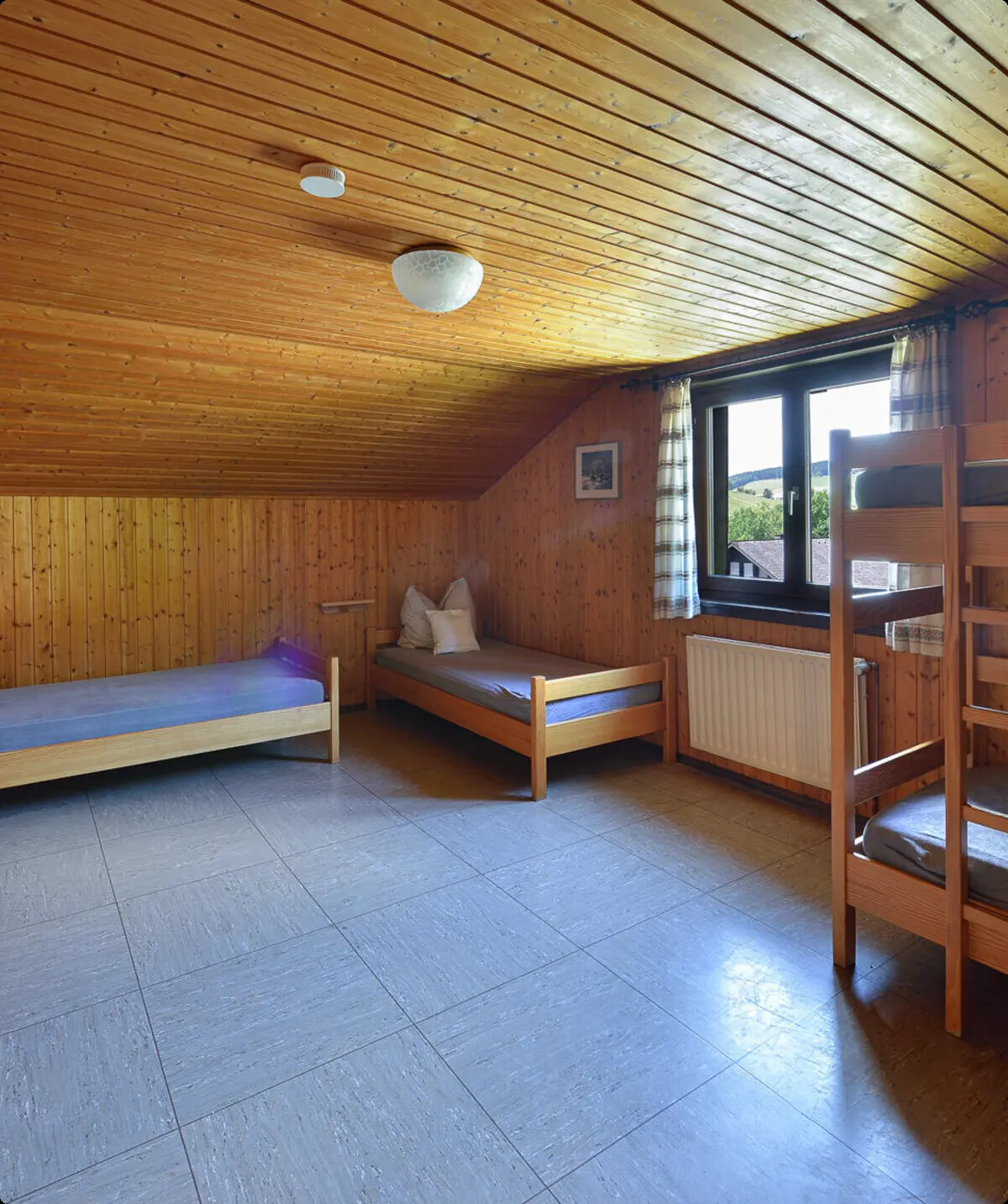 Ein Schlafraum mit Etagenbetten und Einzelbetten, Holzverkleidung und Fenster mit Tageslicht. | © DAV Dortmund
