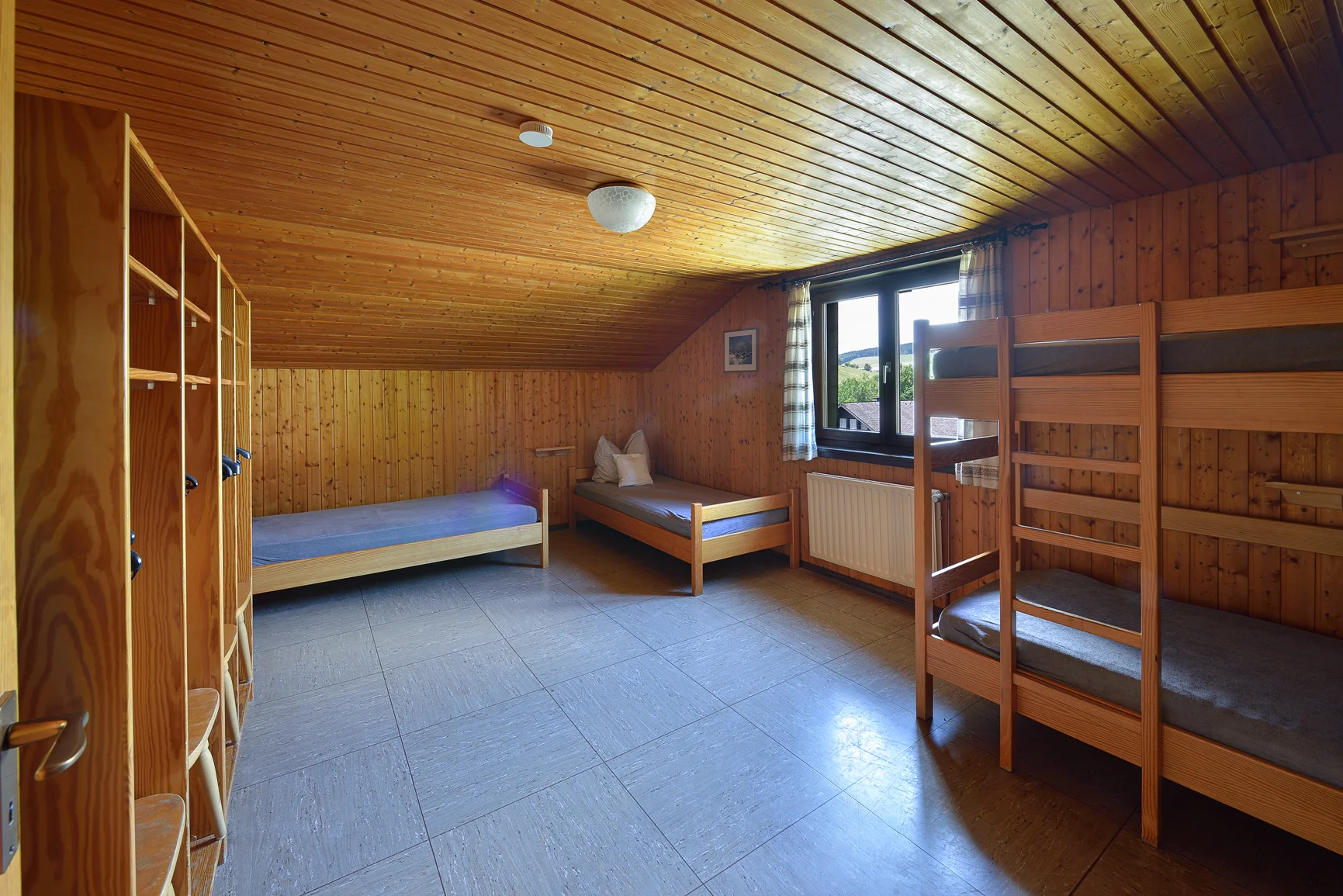 Ein Schlafraum mit Etagenbetten und Einzelbetten, Holzverkleidung und Fenster mit Tageslicht. | © DAV Dortmund