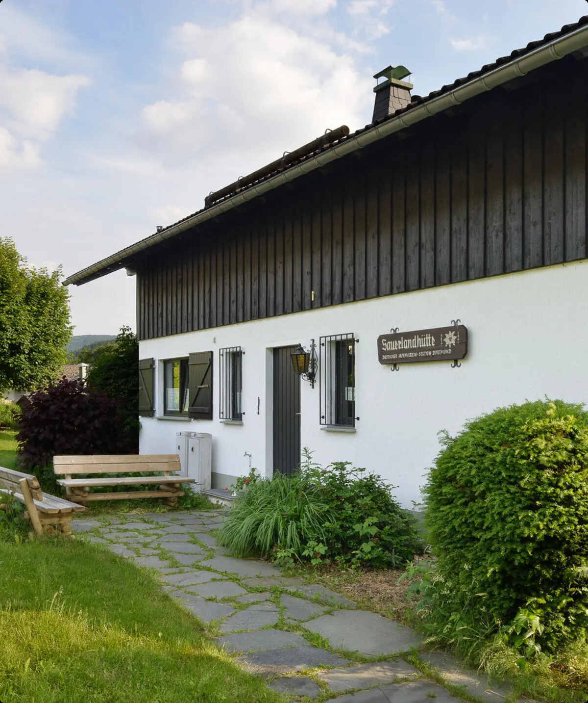 Ein gepflegter Eingangsbereich der DAV-Hütte mit Sitzbank, Blumen und Hinweisschild. | © DAV