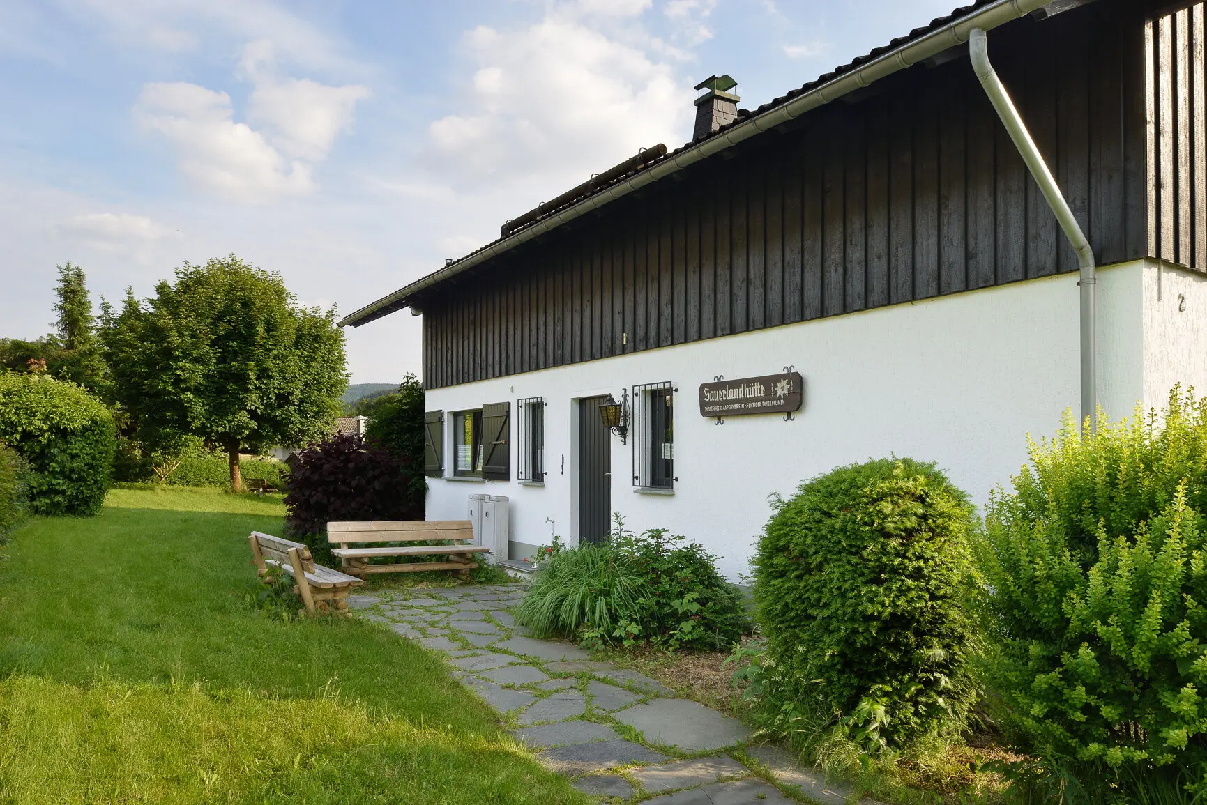 Ein gepflegter Eingangsbereich der DAV-Hütte mit Sitzbank, Blumen und Hinweisschild. | © DAV