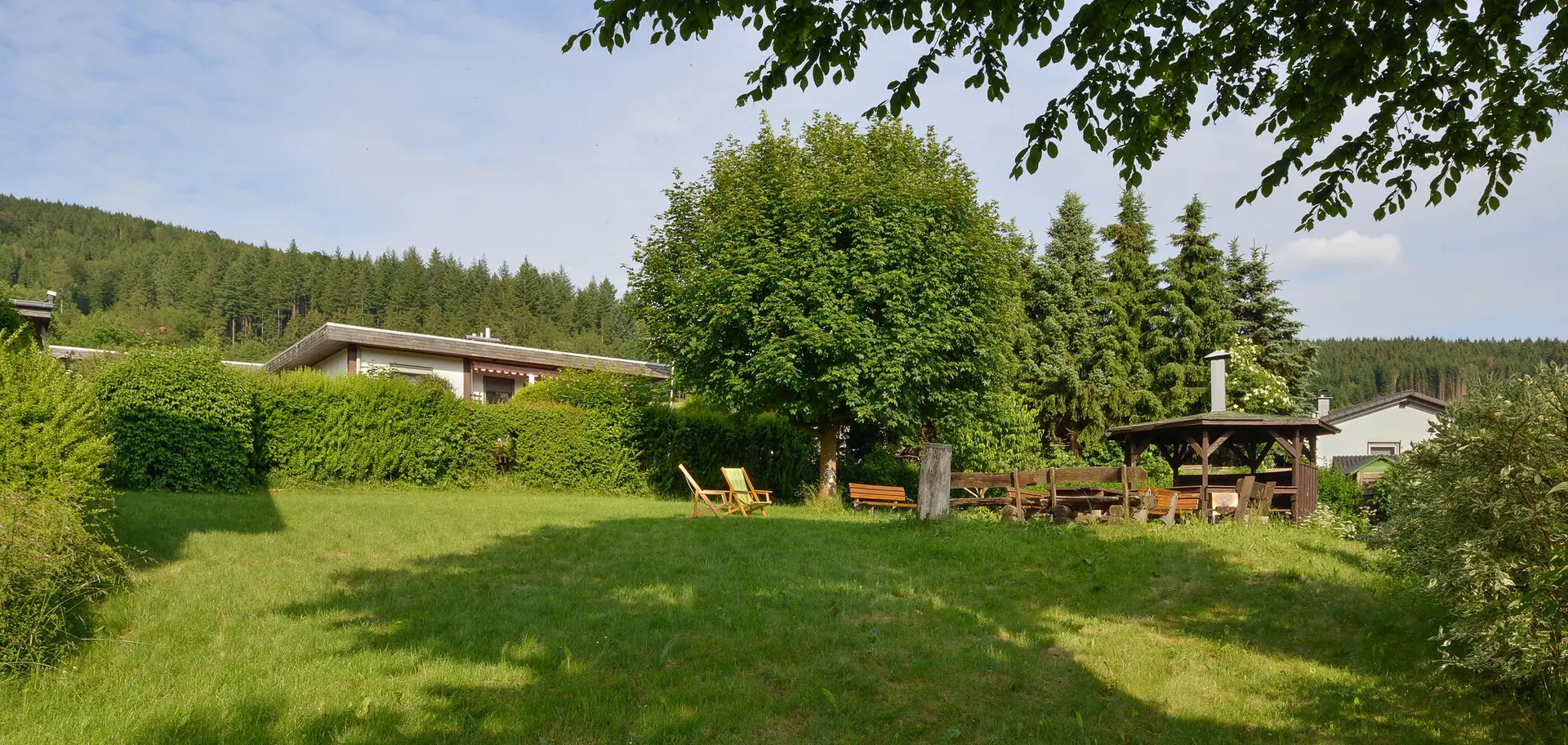 Eine große Wiese mit Bäumen, Sitzgelegenheiten und Grillhütte in ruhiger Lage mit Blick auf den Wald. | © DAV Dortmund