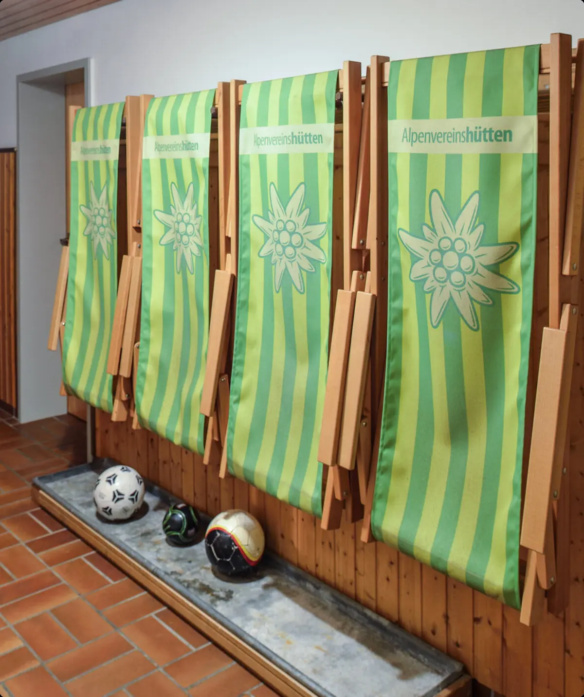 Mehrere grün-gelbe Liegestühle mit Edelweißmotiv stehen ordentlich zusammengeklappt im Innenbereich. | © DAV Dortmund