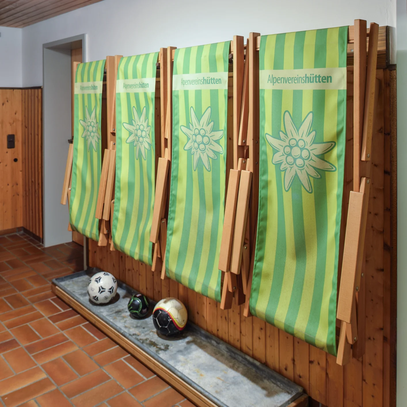 Mehrere grün-gelbe Liegestühle mit Edelweißmotiv stehen ordentlich zusammengeklappt im Innenbereich. | © DAV Dortmund