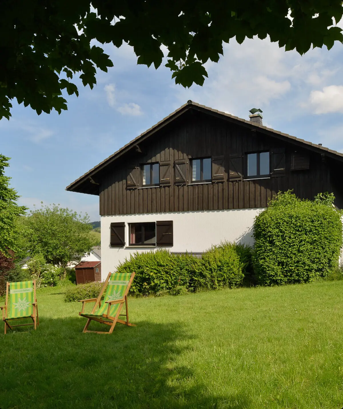 Garten hinter der Hütte mit zwei grünen Liegestühlen und Blick auf Wiese und Bäume. | © DAV Dortmund