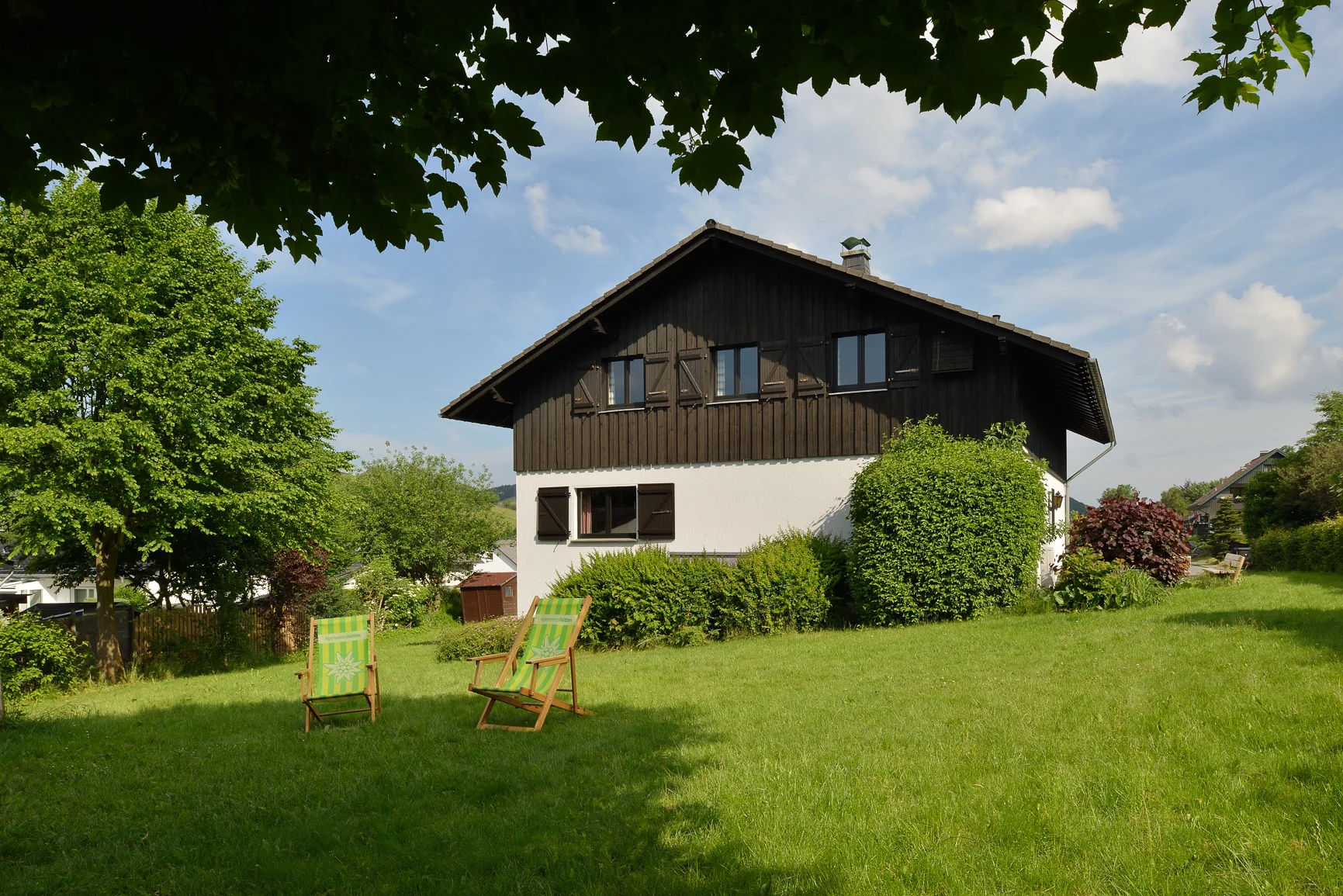 Garten hinter der Hütte mit zwei grünen Liegestühlen und Blick auf Wiese und Bäume. | © DAV Dortmund