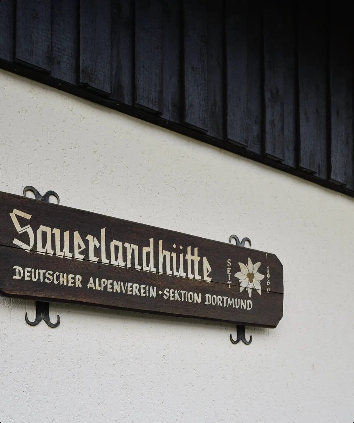 Holzschild an einer Hauswand mit der Aufschrift „Sauerlandhütte – Deutscher Alpenverein Sektion Dortmund“. | © DAV Dortmund