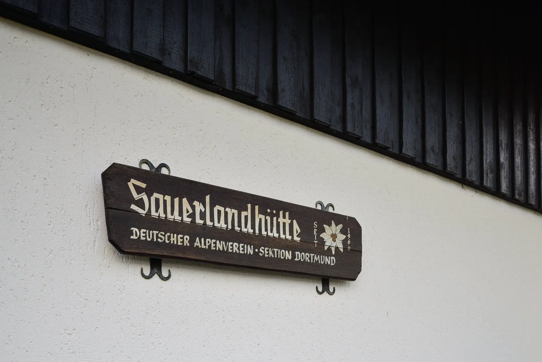 Holzschild an einer Hauswand mit der Aufschrift „Sauerlandhütte – Deutscher Alpenverein Sektion Dortmund“. | © DAV Dortmund