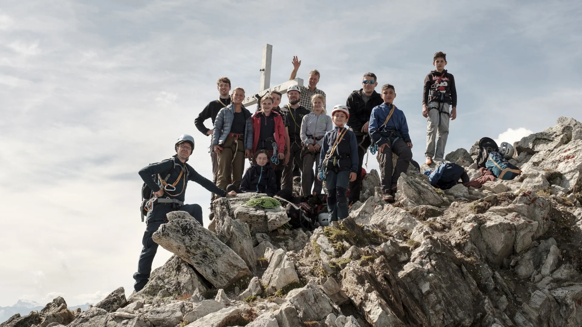 Gruppe von Bergsteiger*innen steht auf einem felsigen Gipfel unterhalb eines Gipfelkreuzes. | © JDAV