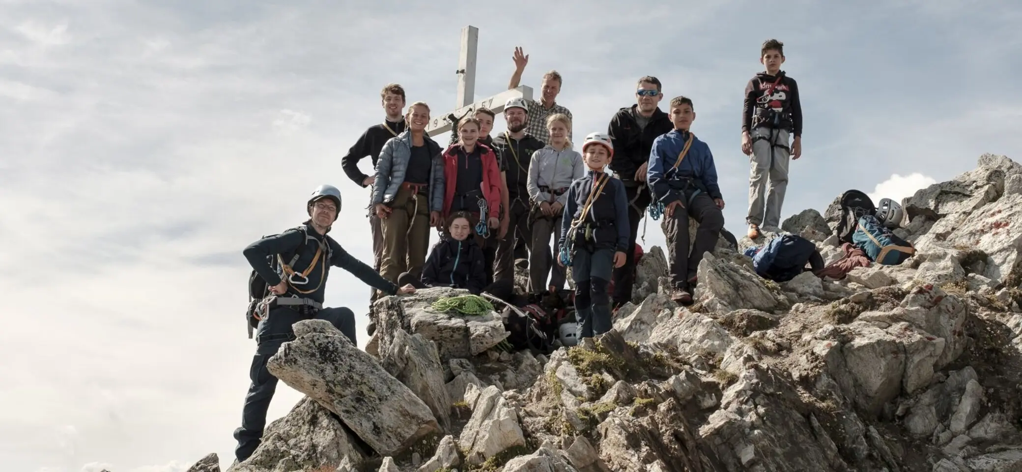 Gruppe von Bergsteiger*innen steht auf einem felsigen Gipfel unterhalb eines Gipfelkreuzes. | © JDAV
