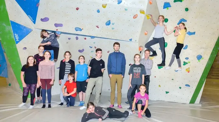 Kinder und Jugendliche posieren in einer Boulderhalle vor einer Kletterwand mit bunten Griffen. | © DAV Dortmund