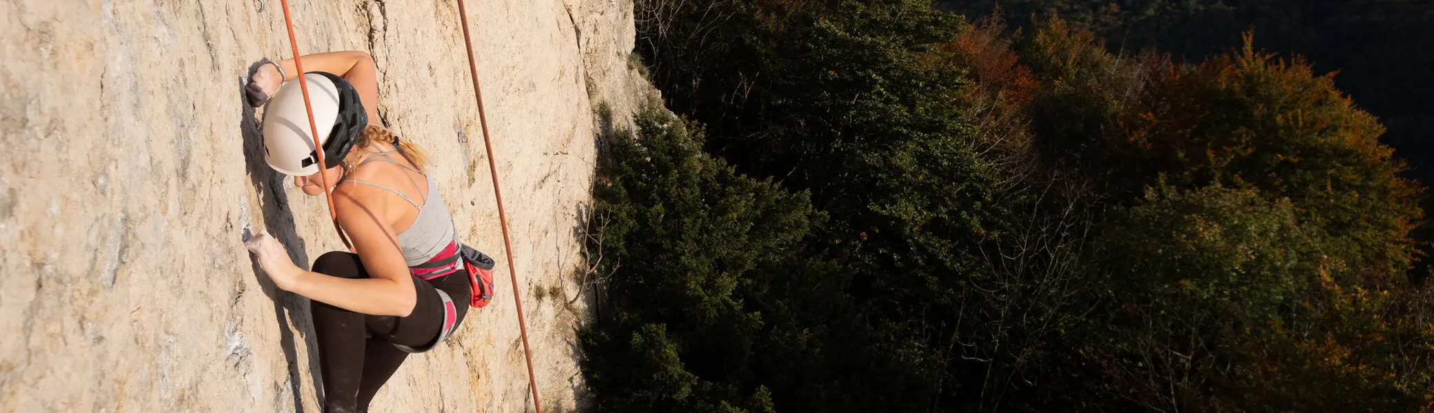 Frau mit Kletterausrüstung klettert an einer Felswand mit Seilsicherung in alpiner Landschaft. | © jdav