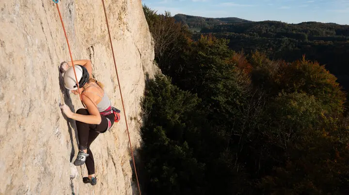Frau mit Kletterausrüstung klettert an einer Felswand mit Seilsicherung in alpiner Landschaft. | © jdav