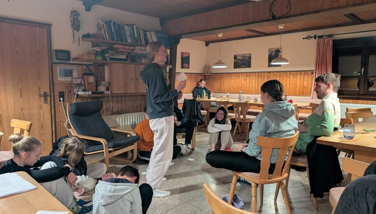 Jugendliche sitzen im Aufenthaltsraum einer Berghütte, eine Person spricht zur Gruppe. | © DAV Dortmund