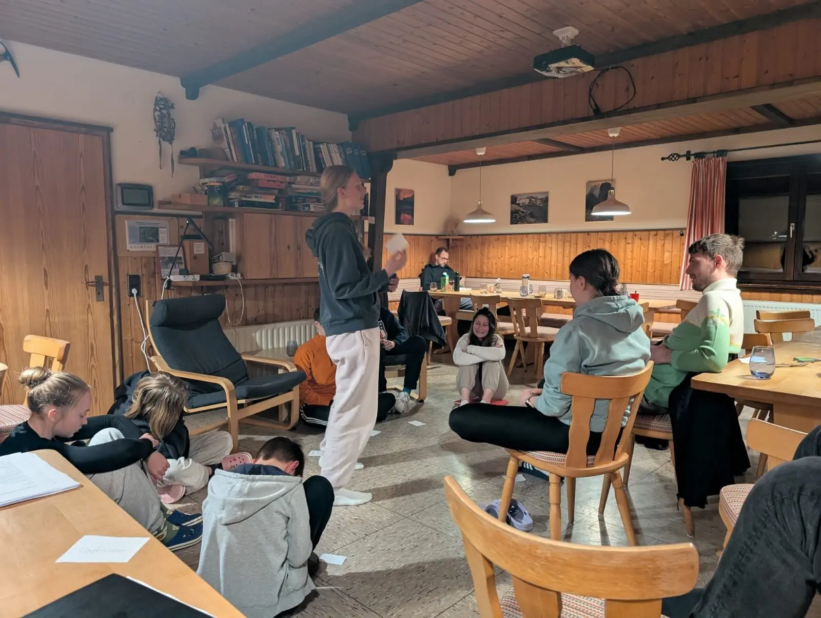 Jugendliche sitzen im Aufenthaltsraum einer Berghütte, eine Person spricht zur Gruppe. | © DAV Dortmund