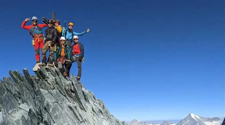     Sechs Bergsteiger*innen jubeln auf einem felsigen Gipfel mit Gletschern im Hintergrund. | © jdav nrw