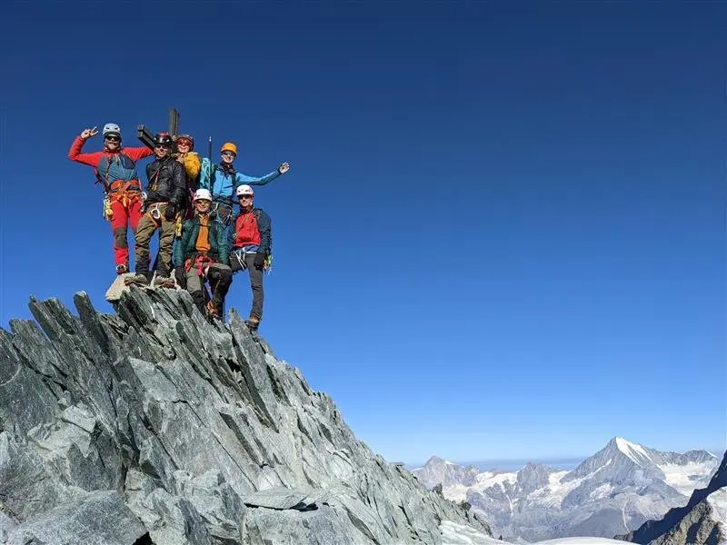     Sechs Bergsteiger*innen jubeln auf einem felsigen Gipfel mit Gletschern im Hintergrund. | © jdav nrw