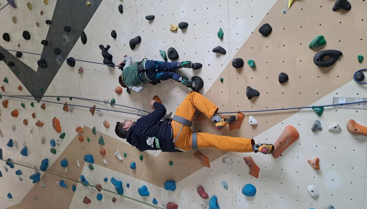 Ein Erwachsener sichert ein Kind beim Klettern an einer Indoorwand mit bunten Griffen. | © DAV Dortmund