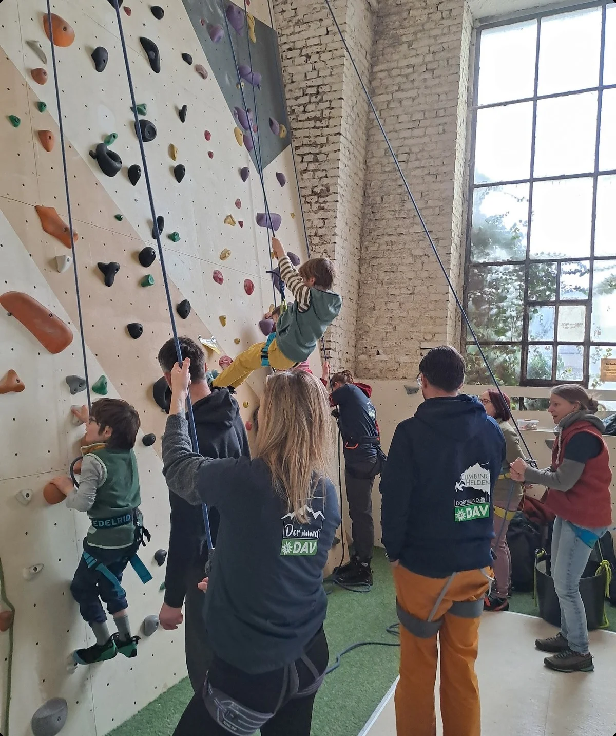 Kinder werden beim Seilklettern an einer Indoor-Kletterwand von Erwachsenen gesichert. | © DAV Dortmund